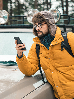 A guy looking at his phone leaning on his hood. 