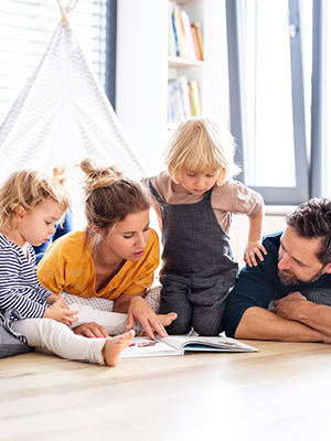 A family of 4 laying on the ground reading a book together